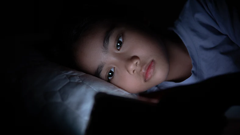 A child gazes at their cellphone while in bed